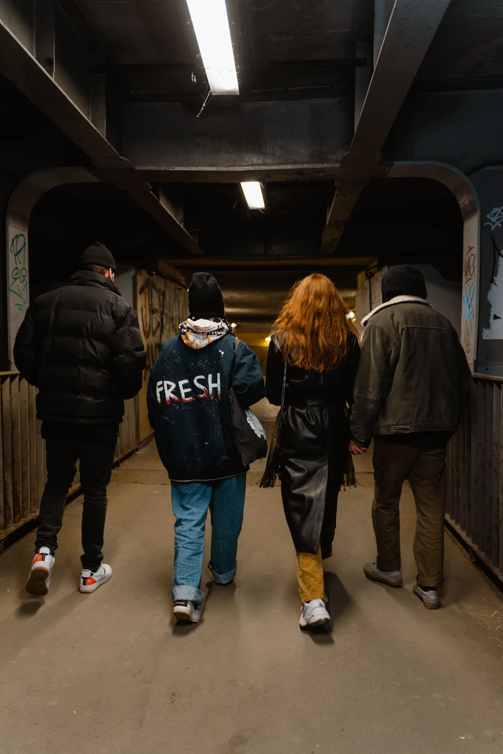 Four friends seen from behind, heading out together through a softly lit urban passage